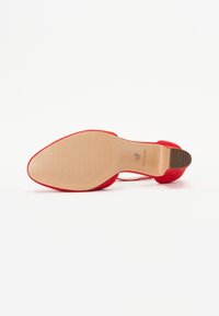 Červená lodička na vysokom podpätku so softsuede vrchom, hladkou podrážkou a špicatou špičkou, ktorá má štíhly podpätok a logo na vnútornej strane.