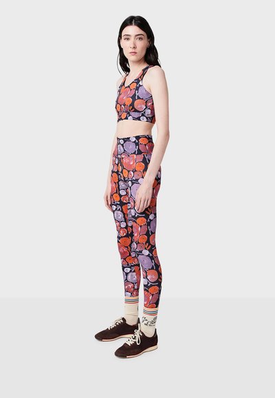 Sada sportovní podprsenky a legín s květinovým vzorem na tmavě fialovém pozadí. Obsahuje červené a levandulové květinové motivy. Bílé kotníkové ponožky s proužky a tmavé boty.