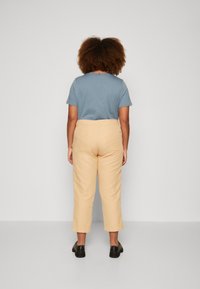 Jasnoniebieska koszulka z krótkim rękawem i beżowe spodenki do kostek wykonane z teksturowanej tkaniny, w połączeniu z czarnymi butami. Widok z tyłu, minimalne detale w designie.