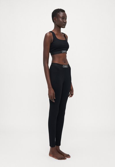 Setul athletic negru include un top cropped ajustat cu bretele groase și colanți prevăzuți cu talie înaltă, ambele având un branding discret la talie.