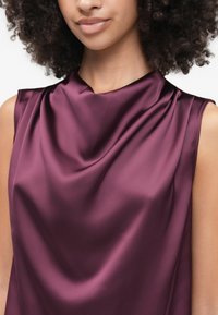 Top senza maniche in satin di un profondo bordeaux con scollo drappeggiato. Il materiale è liscio con una morbida lucentezza e una texture fluida.