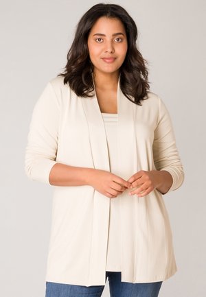 Cremefarbener langer Cardigan mit offenem Vorderteil, weicher Textur und langen Ärmeln, kombiniert mit einem passenden Oberteil und blauen Jeans.