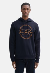 Sudadera azul marino de mezcla de algodón, con un gráfico frontal en naranja que incluye texto y coordenadas, cordones ajustables y puños acanalados.