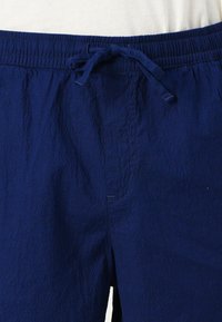 Navy blue shorts with an elastic waistband and drawstring. Textured fabric and side pocket detail visible. Casual design.