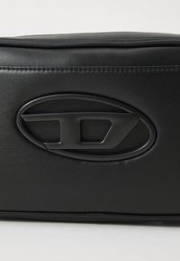 Black synthetic leather bag featuring a prominent oval logo embossed on the front, with smooth texture and subtle stitching detail.