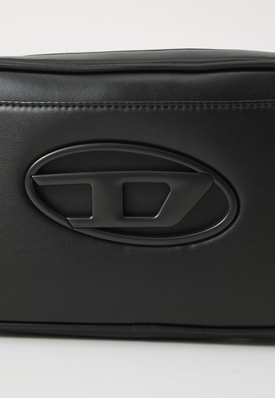 Sac en cuir synthétique noir avec un logo ovale saillant embossé sur l'avant, doté d'une texture lisse et de détails de couture subtils.