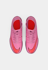 Rózsaszín szintetikus focicipők merész piros Nike logóval. Jellemzők: lapos fűzők, piros belső bélés és fekete talp.