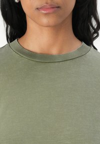 Olijfgroene crew-neck t-shirt gemaakt van een zachte, gestructureerde stof. Heeft een geribbelde halslijn en een casual, fitted snit.