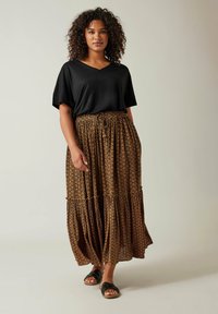 Zwarte v-hals t-shirt gecombineerd met een gelaagde, bruine gemusterde maxi rok. De rok heeft een trekkoord in de taille en wordt aangevuld met zwarte sandalen.