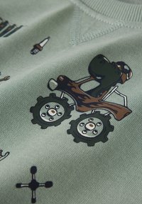 Hellgrüner Stoff zeigt einen Cartoon-Traktor mit großen Rädern, ausgestattet mit einem braunen Körper und einem grünen Fahrer, der eine Schutzbrille trägt.