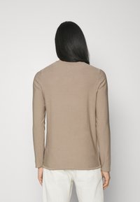 Chemise à manches longues de couleur brun clair, en tissu doux avec un col rond et une coupe droite, présentant un design uni.