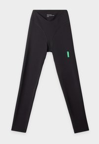 Leggings noirs taille haute avec coutures visibles et petite étiquette verte sur la cuisse droite, posés à plat sur un fond clair.