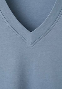 Majica s V-izrezom od mekanog, teksturiranog tkanog materijala svijetloplavih nijansi. Ima čist, kutni izrez s urednim šavovima duž rubova.