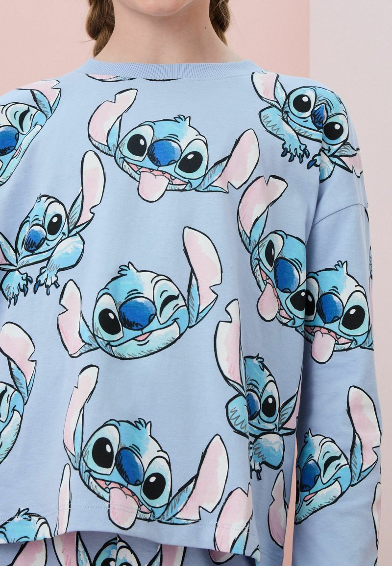 Ljusblå sweatshirt med ett mönster av Stitch, en blå tecknad karaktär, med rosa detaljer och en avslappnad passform.
