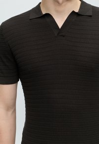 Gros plan d'une personne portant une chemise tricotée noire texturée à manches courtes avec un col en V entaillé.