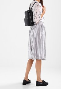 Czarny skórzany plecak o smukłym designie, z komorą na zamek i regulowanymi paskami. Srebrna plisowana spódnica, zestawiona z czarnymi wsuwanymi butami.