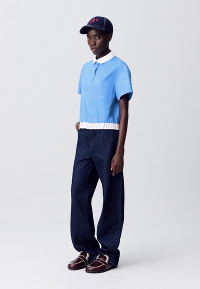 Camisa de manga corta azul claro con cuello blanco y dobladillo plisado, combinada con vaqueros de pierna ancha azul oscuro y zapatos burdeos con detalles plateados.