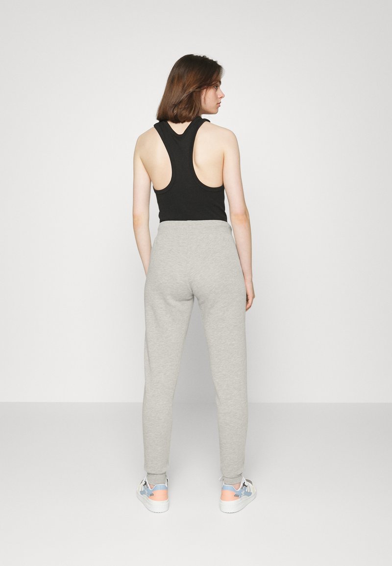Top sin mangas negro tipo racerback, pantalones de chándal ajustados gris claro y zapatillas blancas con acentos en pastel. Tela suave y corte informal.