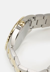 Orologio in acciaio inossidabile con lunetta dorata, corona testurizzata e bracciale bicolore con maglie opache e lucide. Finitura liscia e lucidata.