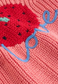 Tissu tricoté rose avec motif fraise rouge et fil bleu formant le mot « amour » à travers la surface.