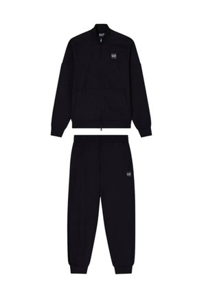 Chaqueta negra con cremallera y cuello alto, acompañada de pantalones jogger a juego que cuentan con cinturilla elástica y parche con logo.