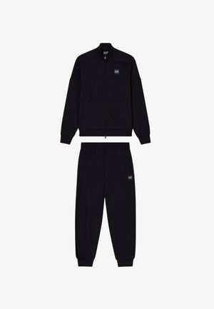 Chaqueta negra con cremallera y cuello alto, acompañada de pantalones jogger a juego que cuentan con cinturilla elástica y parche con logo.