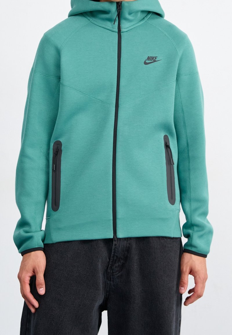 Sudadera con cremallera de Nike en color verde azulado, con capucha, mangas raglán, dos bolsillos laterales con cremallera y un acento de logo negro. Tejido suave y texturizado.