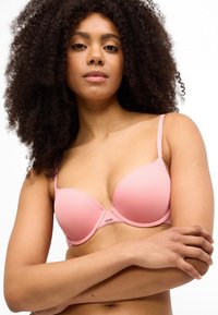 Ανοιχτό ροζ σουτιέν με επένδυση, ρυθμιζόμενους ιμάντες και κεντρικό διακοσ�μητικό στοιχείο, με ομαλό ύφασμα και δομημένο σχέδιο.