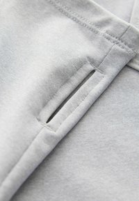 Sivi materijal s mekom teksturom, sa detaljem bočne provale i urednim šavovima. Materijal je lagan i gladak.