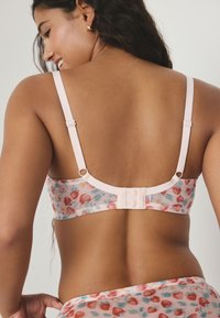 Lyserød blomsterprint bralette med gennemsigtigt stof, justerbare stropper og lukning med tre hægter bagpå. Indeholder jordbær- og bladmotiver.