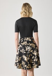 Robe noire avec un haut ajusté et des manches courtes, dotée d'une jupe évasée ornée de motifs floraux dorés. Texture lisse, design contrasté.
