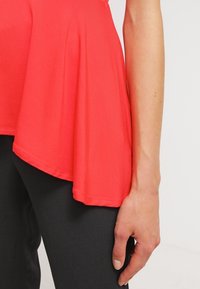 Röd peplumtop med en flödande nederdel och en mjuk textur. I kombination med svarta byxor, som framhäver en slät, åtsittande silhuett.