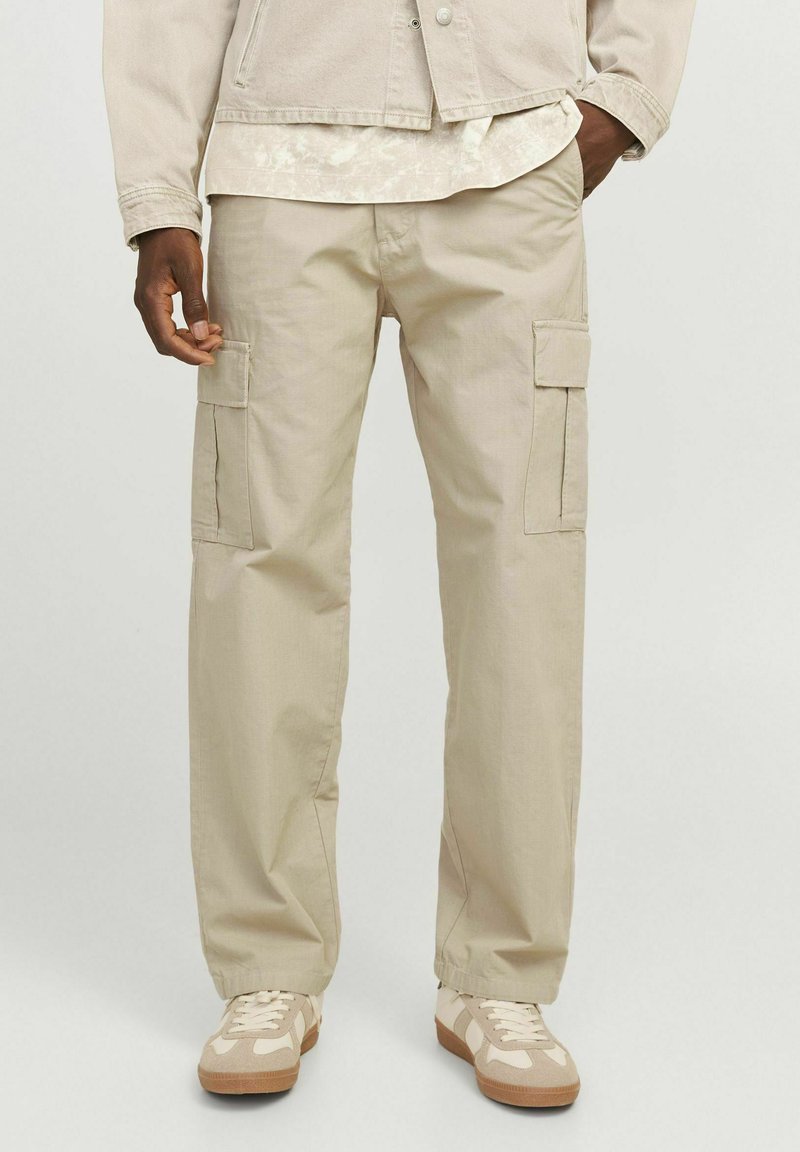Beige cargo bukser lavet af bomuld, med flere lommer, en afslappet pasform og synlige syninger. Båret med beige sneakers.