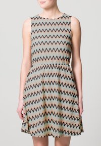 Abito senza maniche con un motivo a zigzag nei toni del beige, nero e teal. La gonna ampia presenta una vita aderente e una trama liscia.