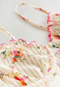 Bloemen tankini-top met lichte stof, crèmekleurige achtergrond, groene strepen, rimpelige roze rand en levendige bloempatroon-details.