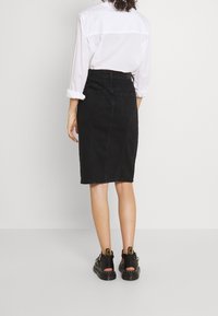 Svart jeanspennkjol med en figurnära design, två bakfickor och knälång fåll, tillsammans med svarta sandaletter med remmar.