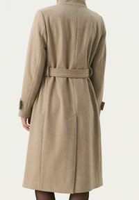 Cappotto in lana beige con vita cintata, maniche lunghe e colletto alto; presenta cuciture dritte e tasche laterali. Vista posteriore mostrata.
