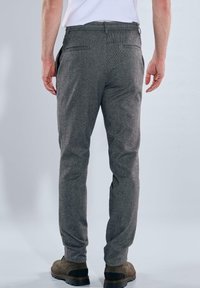 Graue, strukturierte Hosen mit slim fit, ausgestattet mit zwei Gesäßtaschen und einem unauffälligen Bund. Getragen mit braunen Schuhen.