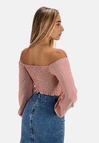 Top rosa off-shoulder con corpetto arricciato e maniche lunghe, abbinato a una gonna di jeans a vita alta con zip frontale e silhouette aderente.