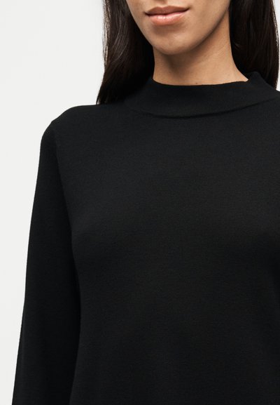 Μαύρο πλεκτό πουλόβερ με ψηλό λαιμό και μακριά μανίκια. Το ύφασμα φαίνεται απαλό με λείο υφή και ελάχιστες λεπτομέρειες.