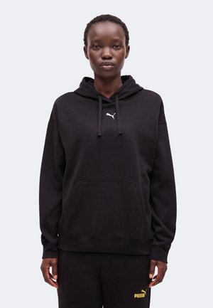 Osoba nosi čiernu kapucňu s malým bielym logom Puma a čierne nohavice so žltým logom Puma na ľavom stehne.
