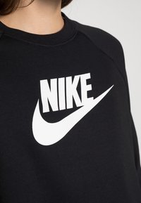 Person wearing a black sweatshirt with a large white Nike logo centered on the chest against a plain background.