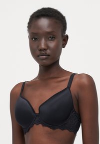 Black bra with smooth padded cups and lace detailing at the band. Adjustable straps with a delicate lace edge.