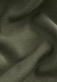 Tissu texturé vert foncé avec un motif tissé serré, montrant de doux plis et des ombres subtiles.