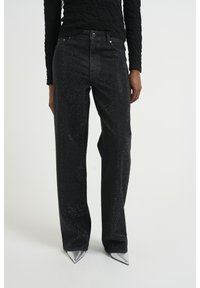 Jeans de mezclilla negra con corte recto, adornados con tachuelas plateadas para un aspecto texturizado. Combinados con zapatos de tacón metálicos puntiagudos.