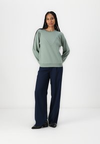 Suéter verde claro con mangas abullonadas, diseño en forma de V, combinado con pantalones de pierna ancha azul marino y zapatos negros brillantes. Conjunto sencillo y moderno.