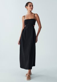 Must maxi kleit, millel on istuv bodi, reguleeritavad õhukesed rihmad ja küljes lõiked. Valmistatud siledast kangast voolava siluetiga.