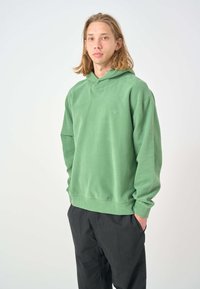 Green cotton hoodie with a relaxed fit, kangaroo pocket, and ribbed cuffs. Features a small blue bird emblem on the chest.