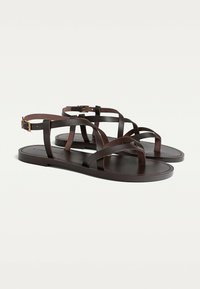 Brune lædersandaler med flere tynde stropper, flad sål og en lille spænde detalje på ankestroppen. Glat tekstur, minimalistisk design.