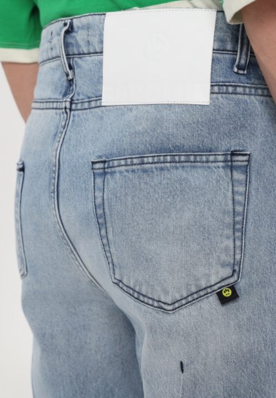 Lichtblauwe denim jeans met een hoge taille, voorzien van twee achterzakken, een wit leren logopatch en een klein zwart label met een geel logo.